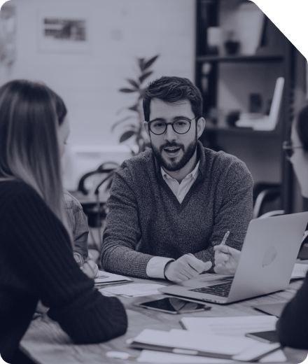 Man wearing glasses working with laptop in a modern office environment with plants and documents visible